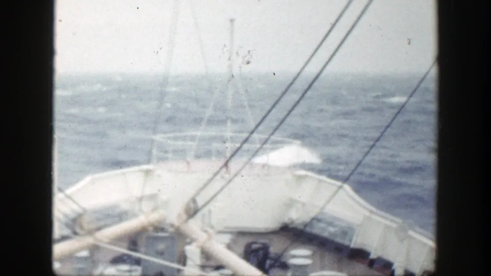 Shipboard 8mm frame showing railings, rigging lines, and choppy ocean under a hazy sky.