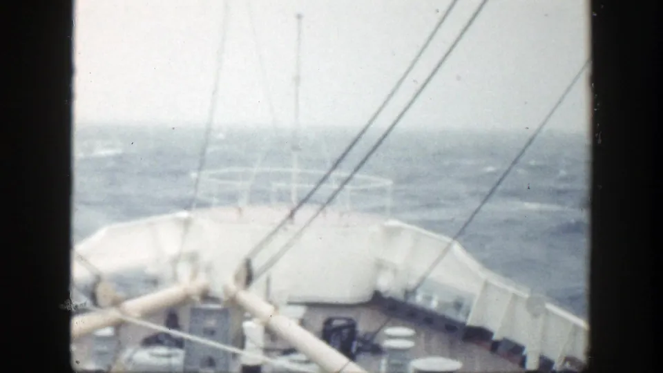 A soft, bright ship-deck view shows the bow, railings, rigging, and turbulent ocean beyond.