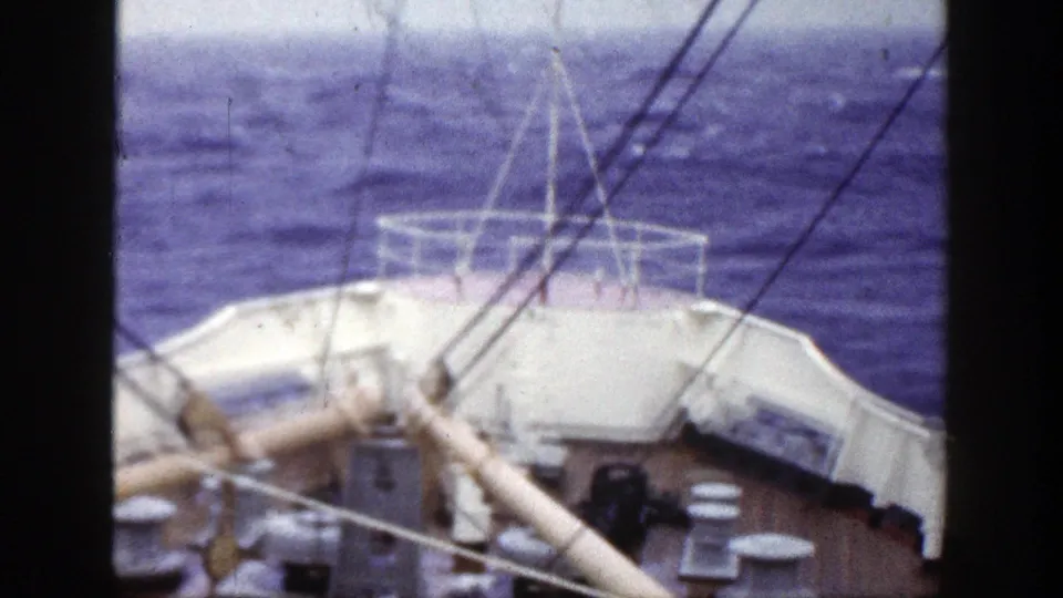 Ship bow and rigging fill the foreground while darker blue waves and white spray roll ahead.