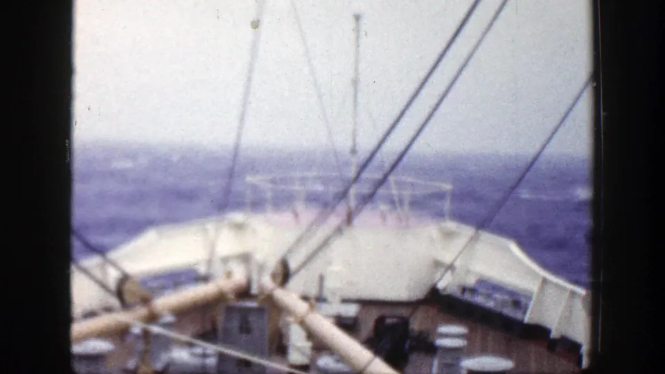 1948 8mm frame from a ship deck, with railings, angled rigging, and rough seas under an overcast sky.