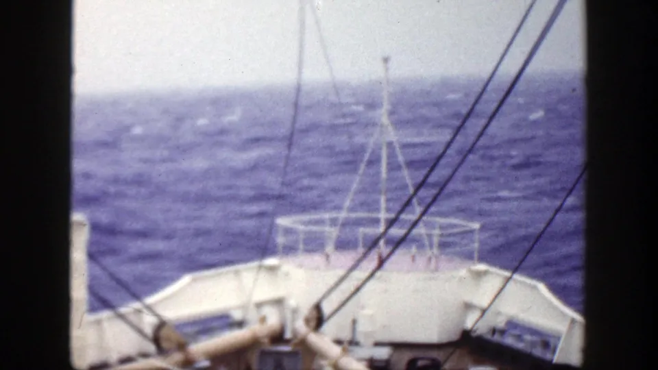 Late-1940s 8mm deck view with white bow railings, dark rigging lines and choppy blue sea ahead.