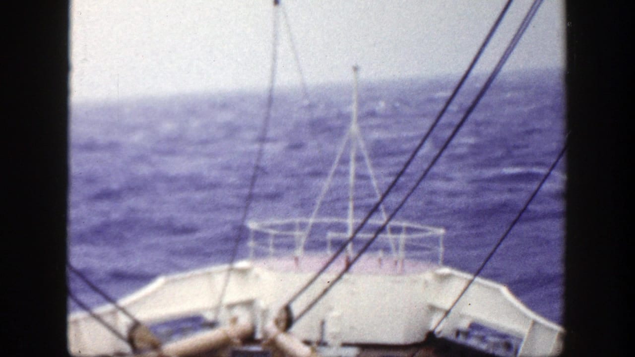 1948 New York 8mm frame showing a forward boat-deck view over mildly wavy blue water, with white railing and rigging lines visible.