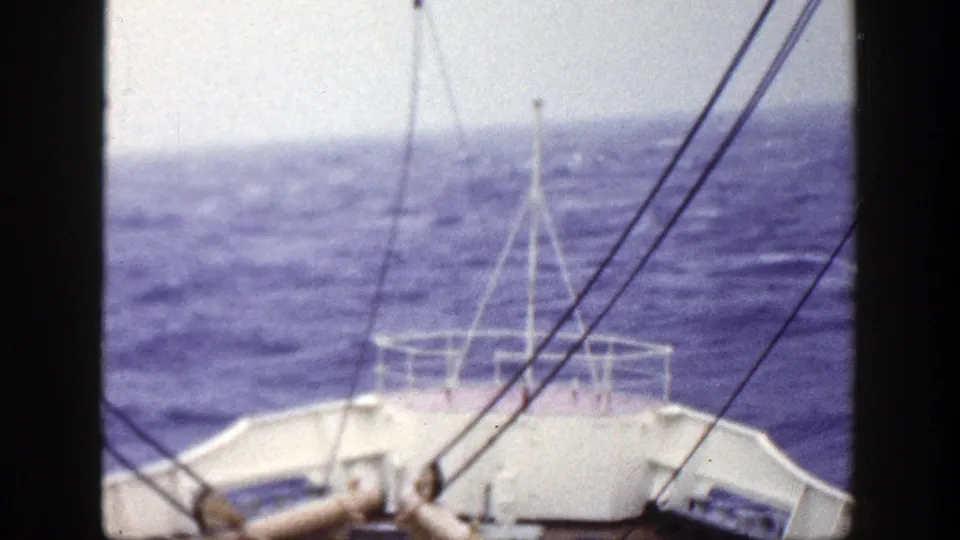 1948 New York 8mm frame showing a forward boat-deck view over mildly wavy blue water, with white railing and rigging lines visible.