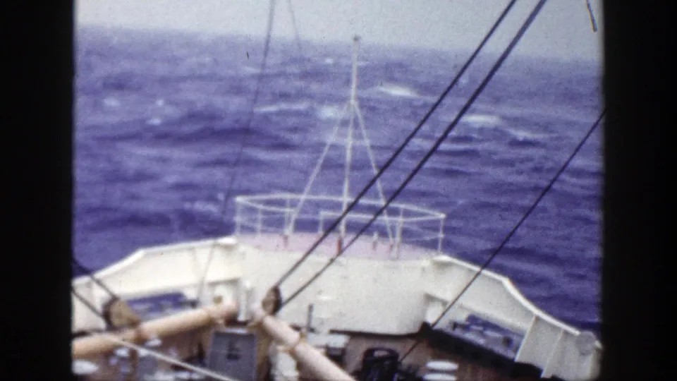 A forward-facing 8mm view from a boat deck in 1948 New York, with white bow railings, rigging, and choppy blue water ahead.