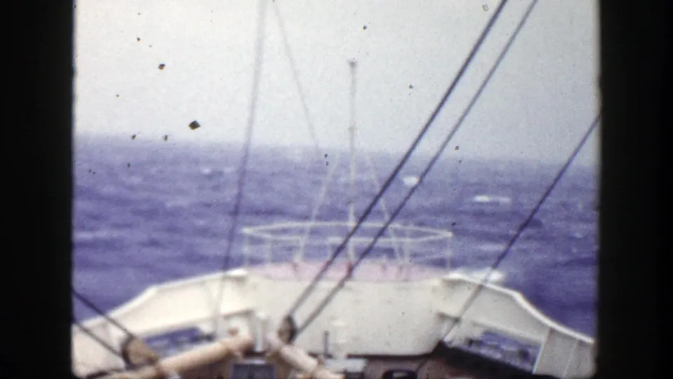 Final 8mm frame of the boat bow and railings looking out across choppy blue water, with visible dust specks and dark frame borders.