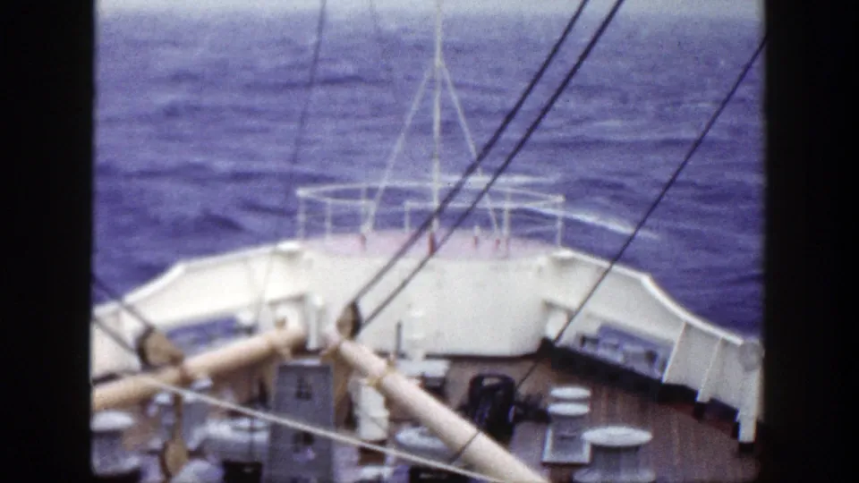 The ship's bow and railings appear from a handheld 8mm deck view as the ocean rolls ahead.