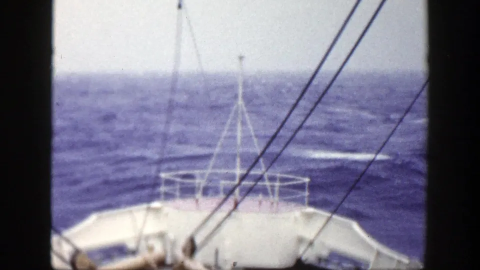 A 1948 home-movie frame looks past ship rigging and bow rail toward a rough open sea.