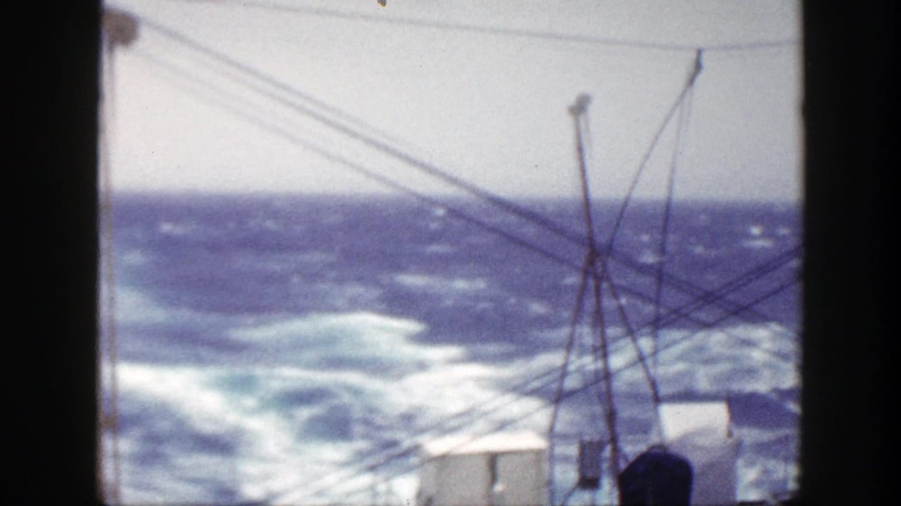 Rough blue ocean with whitecaps seen past ship rigging and dark frame edges.