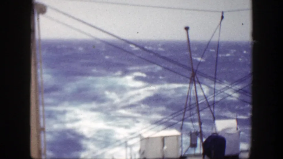 Rough ocean waves under a pale cloudy sky, filmed from a 1948 shipboard viewpoint with rigging and deck shapes in front.