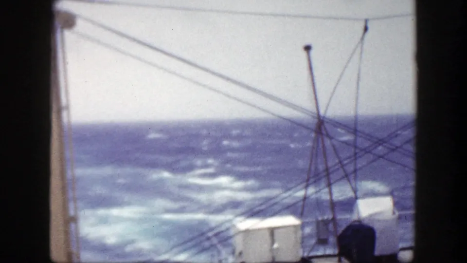 Late-1940s 8mm shipboard view of a rough ocean horizon, with whitecaps, rigging lines, and deck hardware in front.