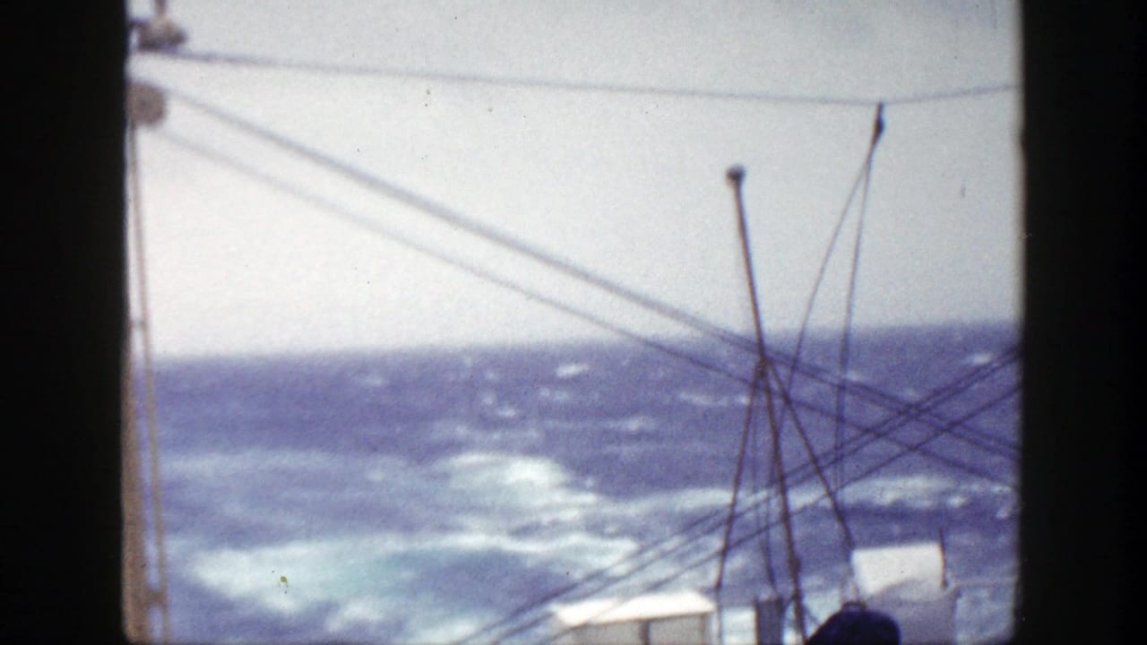 Choppy blue ocean seen past ship rigging and dark film-frame borders.