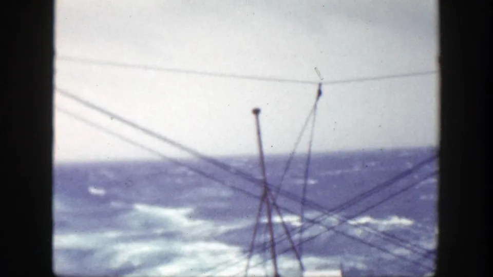 Shipboard 8mm view of rough seas near New York, with whitecaps beyond crisscrossing rigging and vertical film-frame edges.