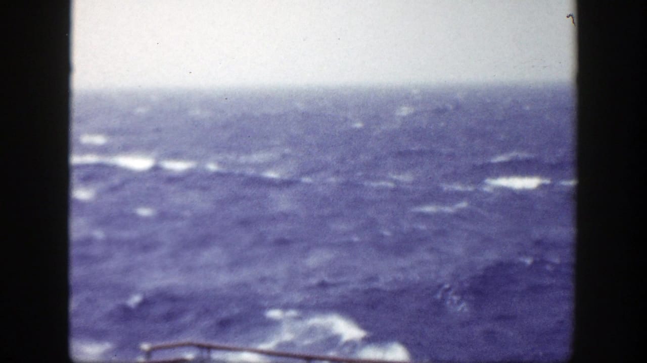 Choppy blue ocean with whitecaps seen through dark vertical deck framing.