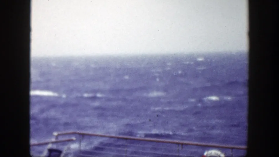 Rough seas off New York in 1948, with a metal railing and partial red-and-white life preserver visible from the vessel deck.