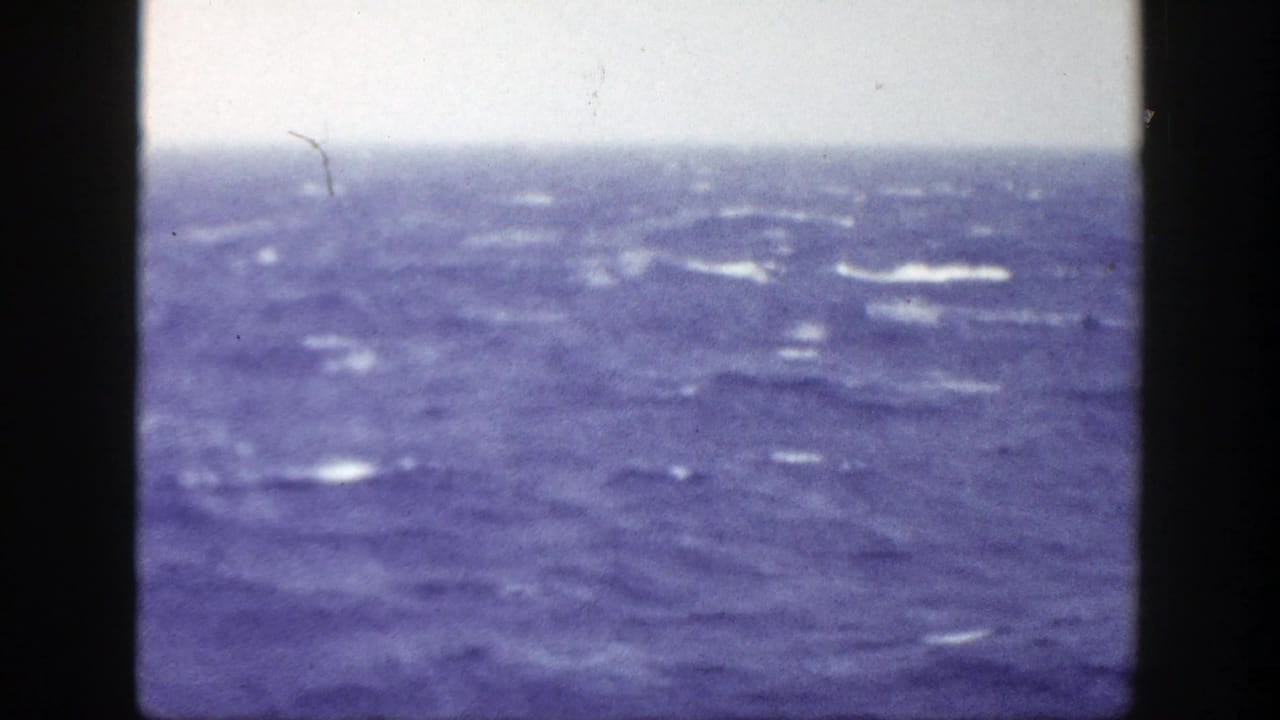 Choppy blue ocean beneath an overcast sky, framed by dark film borders.
