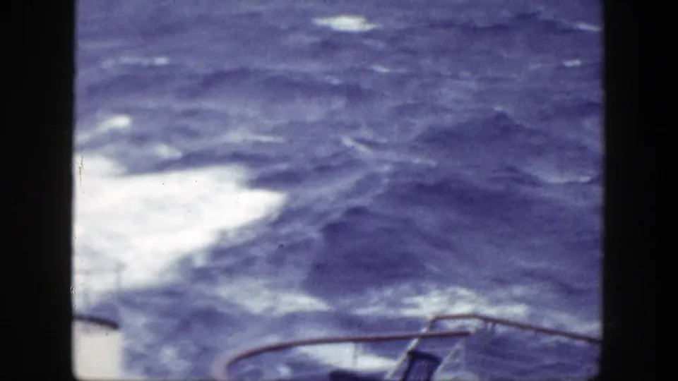 1948 8mm home-movie view of rough blue water and white foam, with ship railing and a deck chair partly visible below.