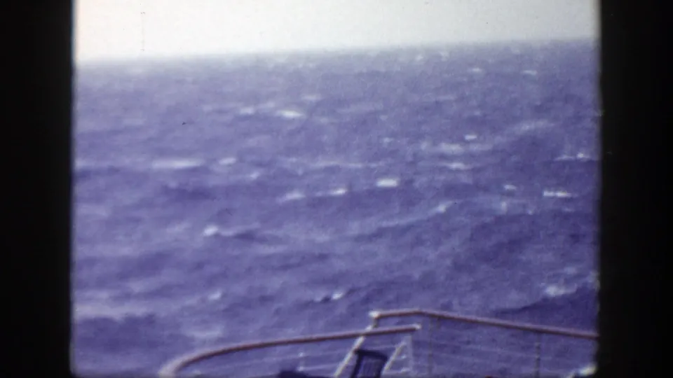 1948 8mm frame looking over a boat rail toward rolling water, with a deck chair partly visible below.