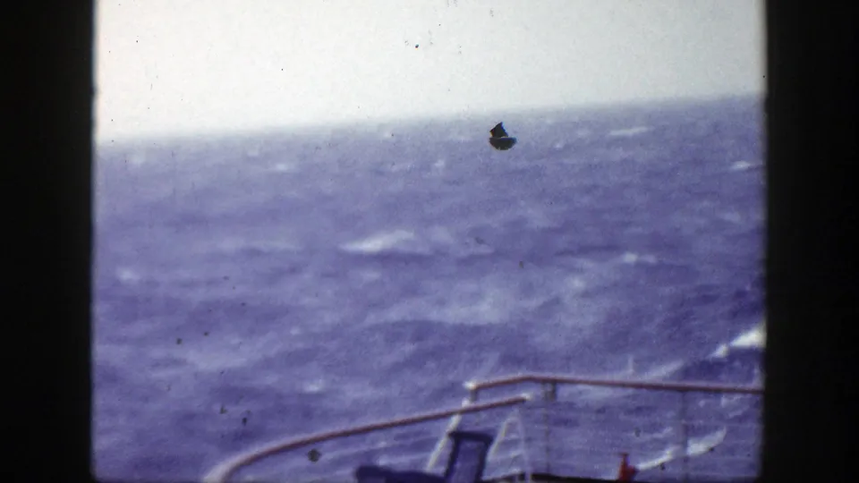 Handheld 8mm view of rough water from a boat, with the rail and a chair edge framing the lower foreground.