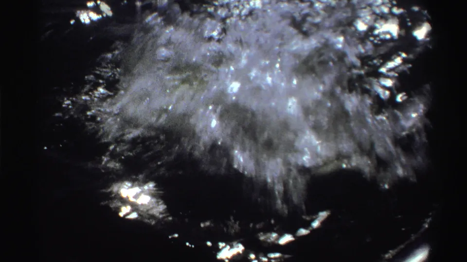 1969 Nigeria 8mm frame showing turbulent water beside a small boat during a fishing catch, with bright sun glare and dark handheld framing.