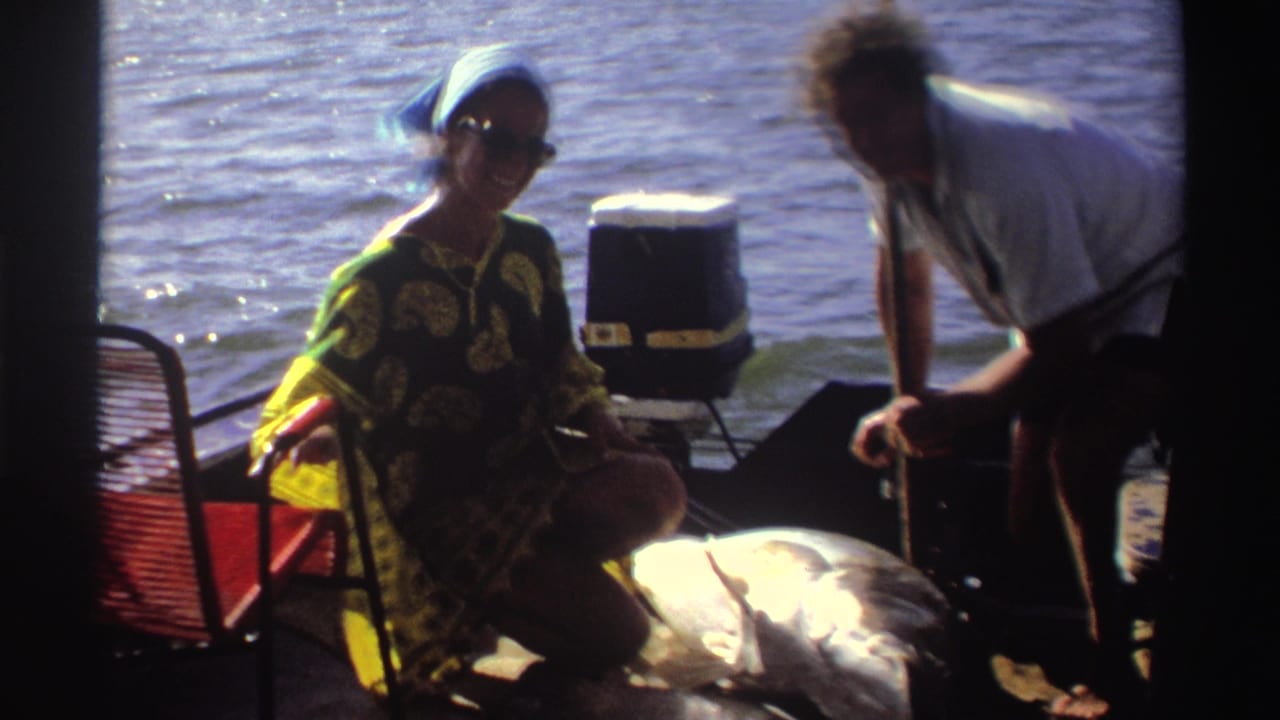 Adults on a small boat beside river water, with a woman holding a large fish.