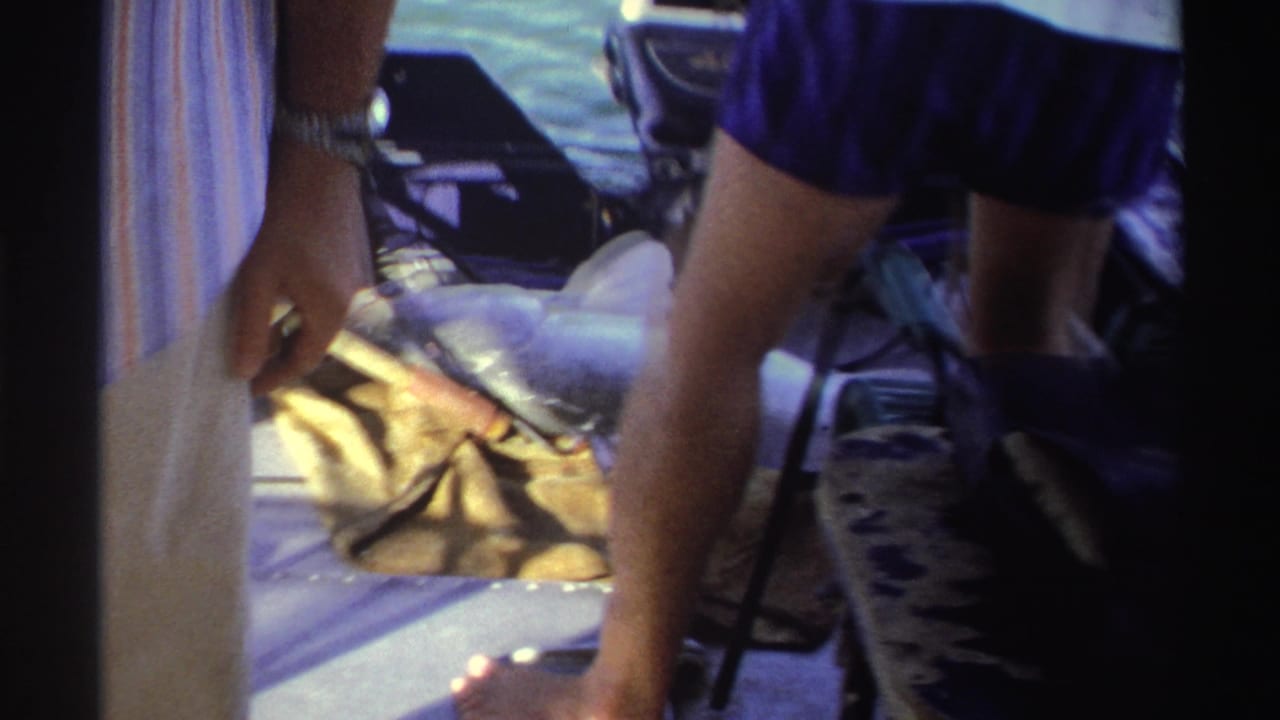 1969 Nigeria frame showing adults around a large grey and white fish resting on the deck of a small boat.