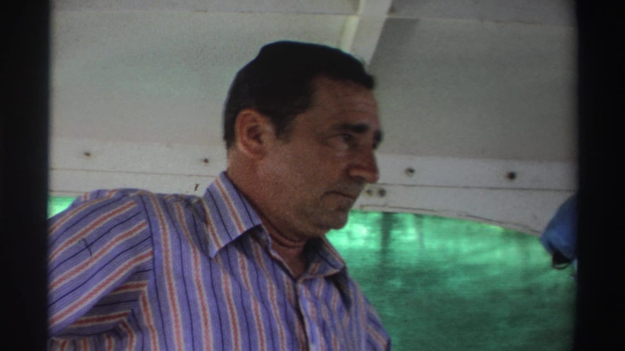 1969 Nigeria home-movie frame of a man in a striped shirt aboard a boat, filmed close up with water outside.