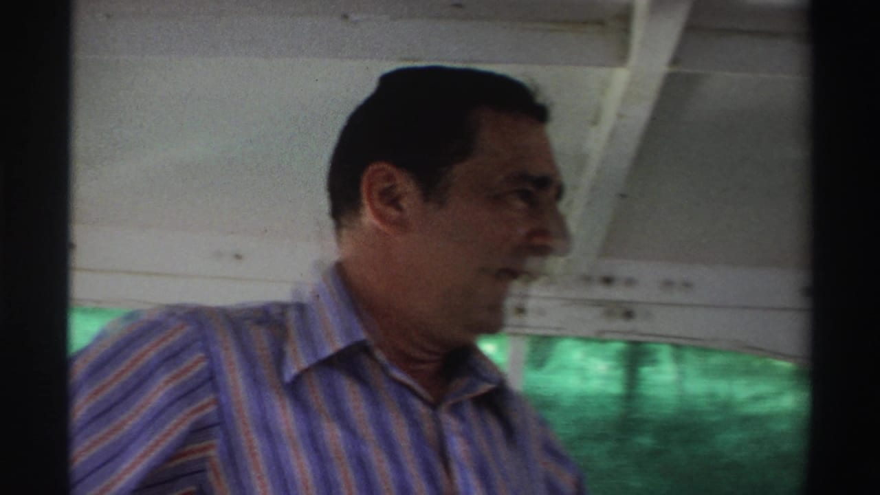1969 Nigeria boat frame showing a man in a striped shirt in profile, with the vessel interior and green water behind him.