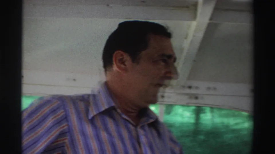 1969 Nigeria boat frame showing a man in a striped shirt in profile, with the vessel interior and green water behind him.