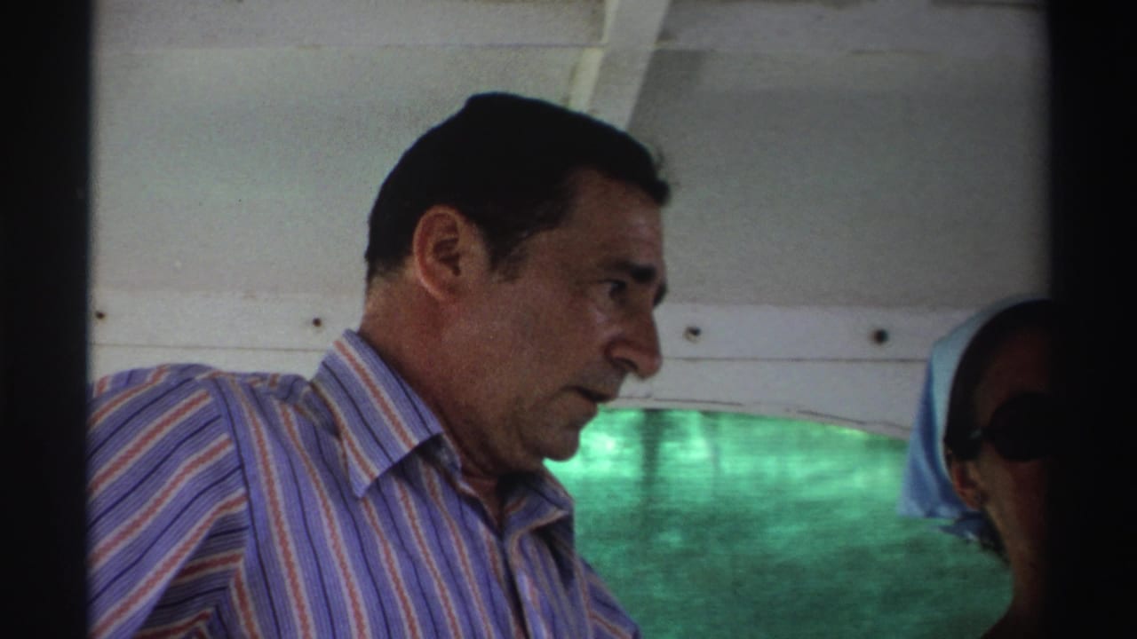 In Nigeria, 1969, the man looks down aboard the boat while another passenger in sunglasses is partly visible behind him.