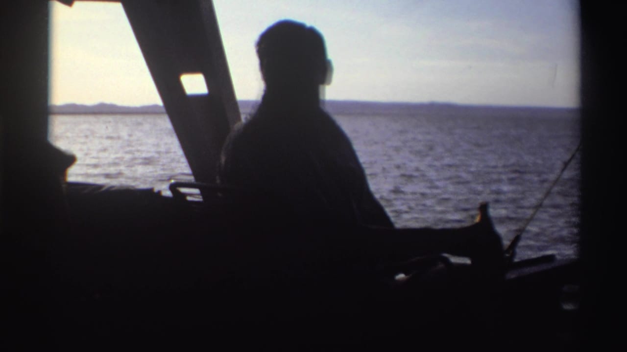 1969 Nigeria 8mm still of a man seen in silhouette from inside a boat, looking toward open water and distant land.