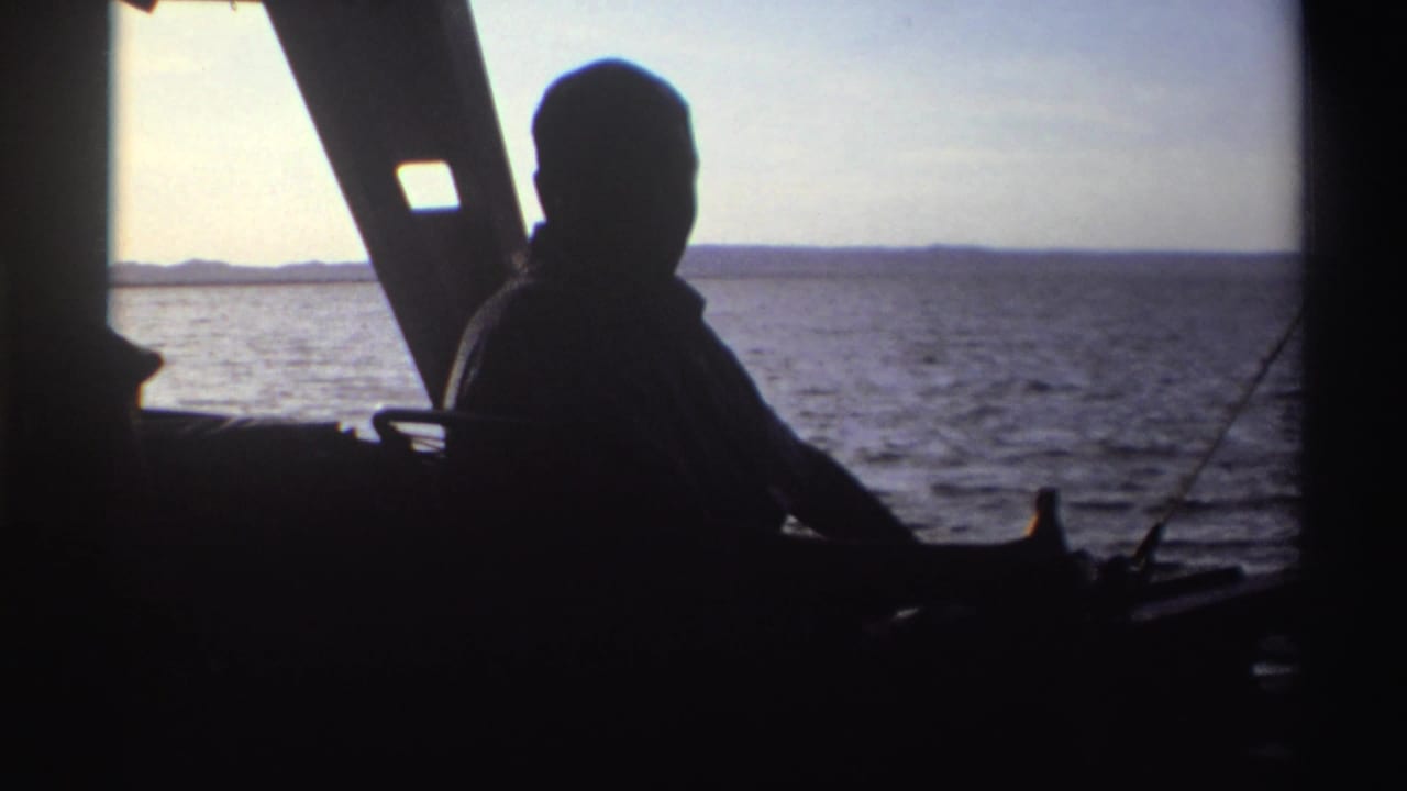 The silhouetted man remains seated on the boat, partly turned toward the camera with water and horizon behind him.