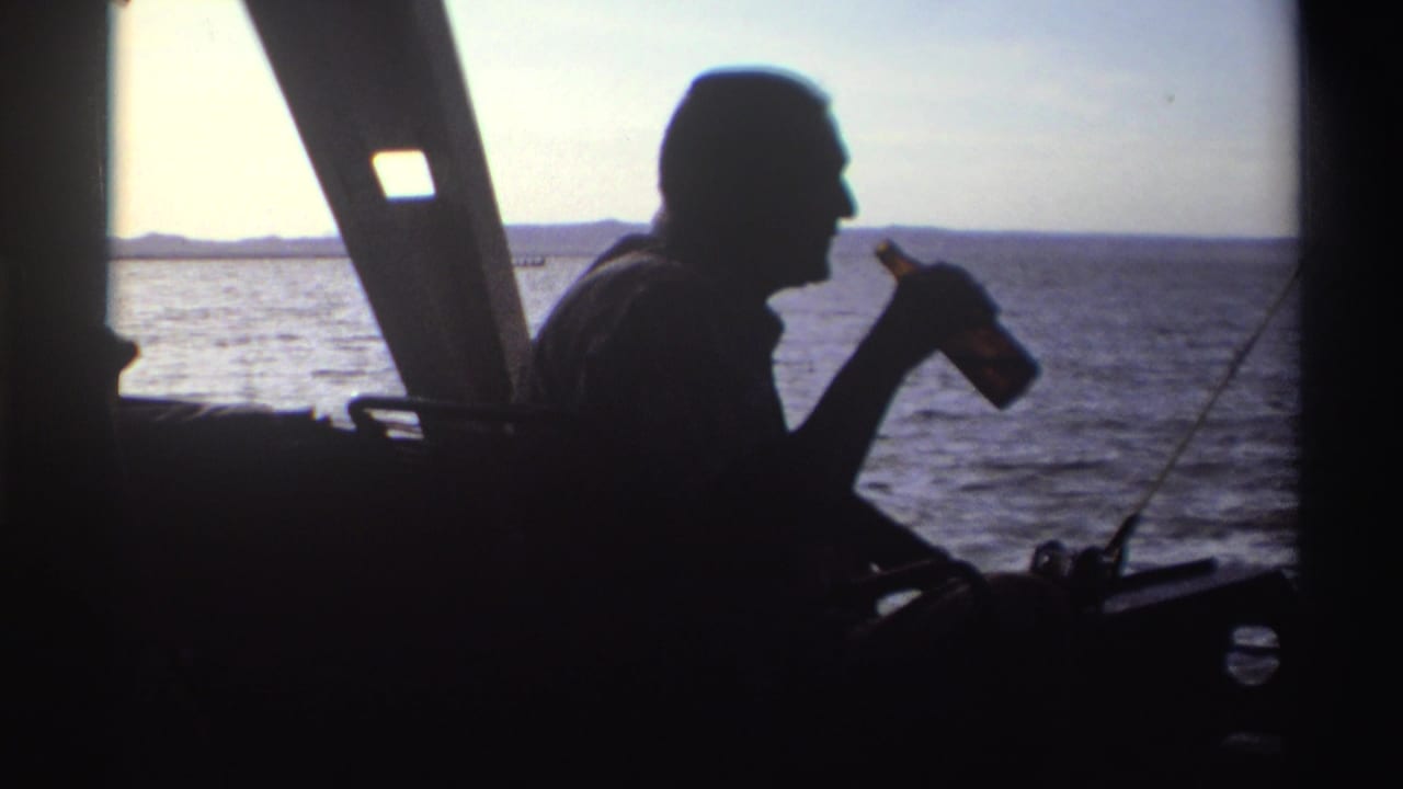 The man raises a bottle near his mouth while seated in silhouette on the boat, with Nigerian waters visible beyond.