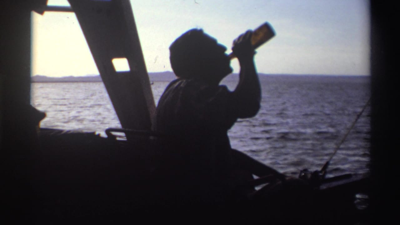 A silhouetted man drinks from a bottle aboard the boat, framed by bright water, sky, and a dark structural support.