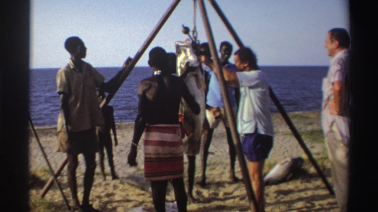 Nigeria, 1969: adults stand on a beach beside a large fish being lifted with a wooden tripod and pulley near the sea.
