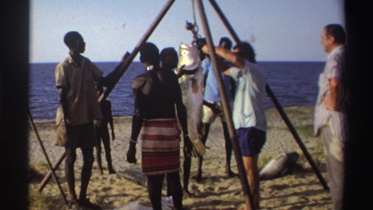 Nigeria, 1969: men work around a tripod pulley as a large fish hangs above the sand, with the ocean behind them.