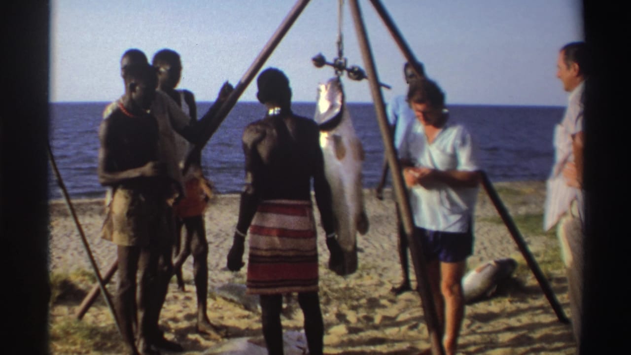 Nigeria 1969 8mm frame showing adults near the shoreline, including a large fish hanging from a wooden tripod on the sand.