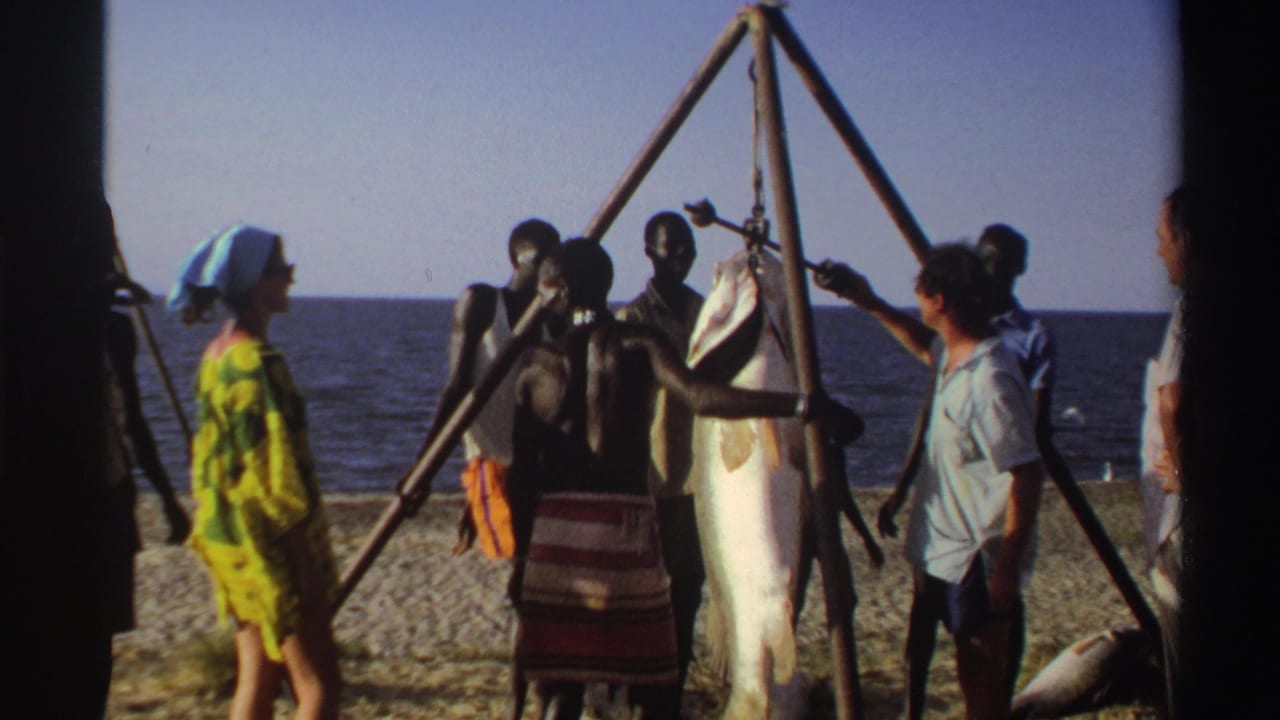 Late-1960s Nigeria beach footage shows adults gathered around a large fish hanging from a wooden tripod near the shoreline.