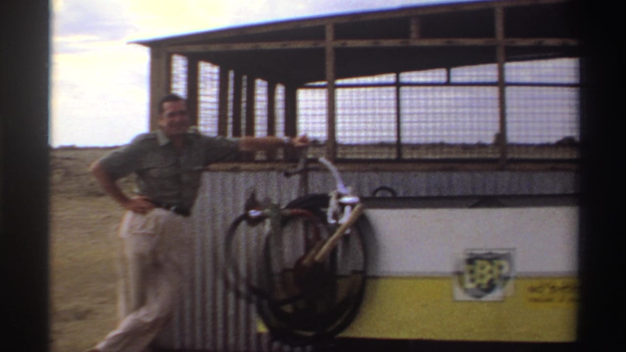 The man poses beside a corrugated shelter with bicycle parts and a BP-branded container visible in the lower right.