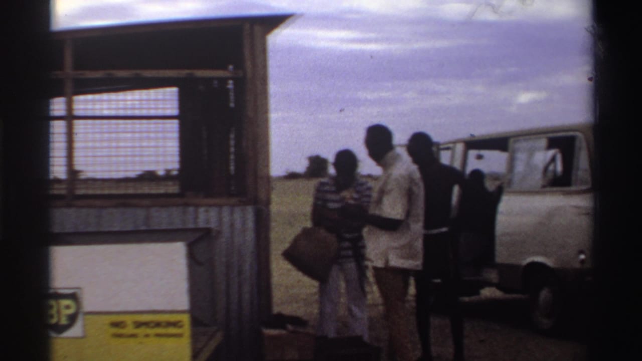 Travelers in 1969 Nigeria stand with bags beside a BP fuel station while a white van waits on the open airstrip.