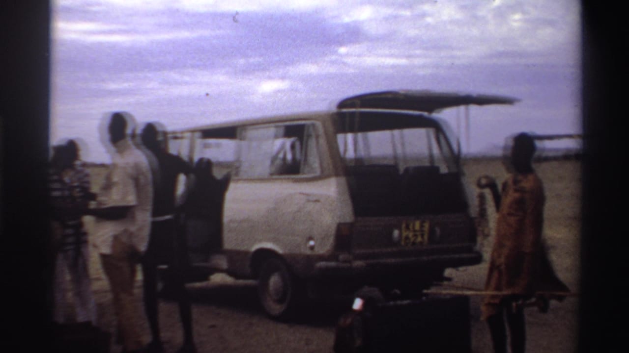 At a Nigeria airstrip in 1969, travelers stand by an open white van as another person carries luggage across the foreground.