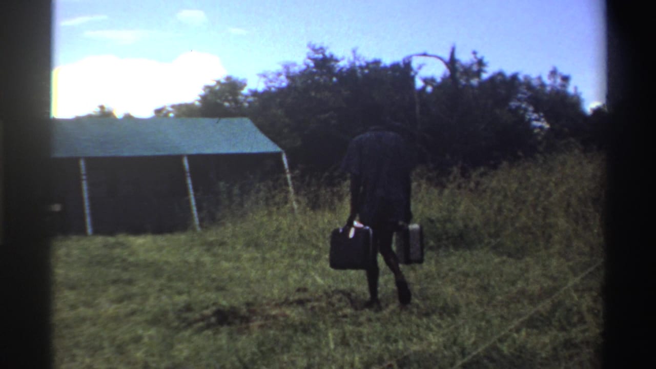 Man with suitcases walks away from the camera toward a green-roofed tent.