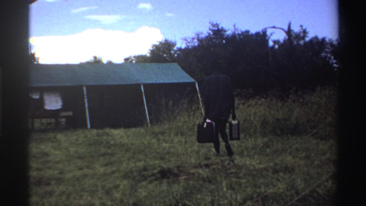 In the later frame, the man appears farther away with both suitcases, near tall grass and the tent in a rural Nigeria setting.