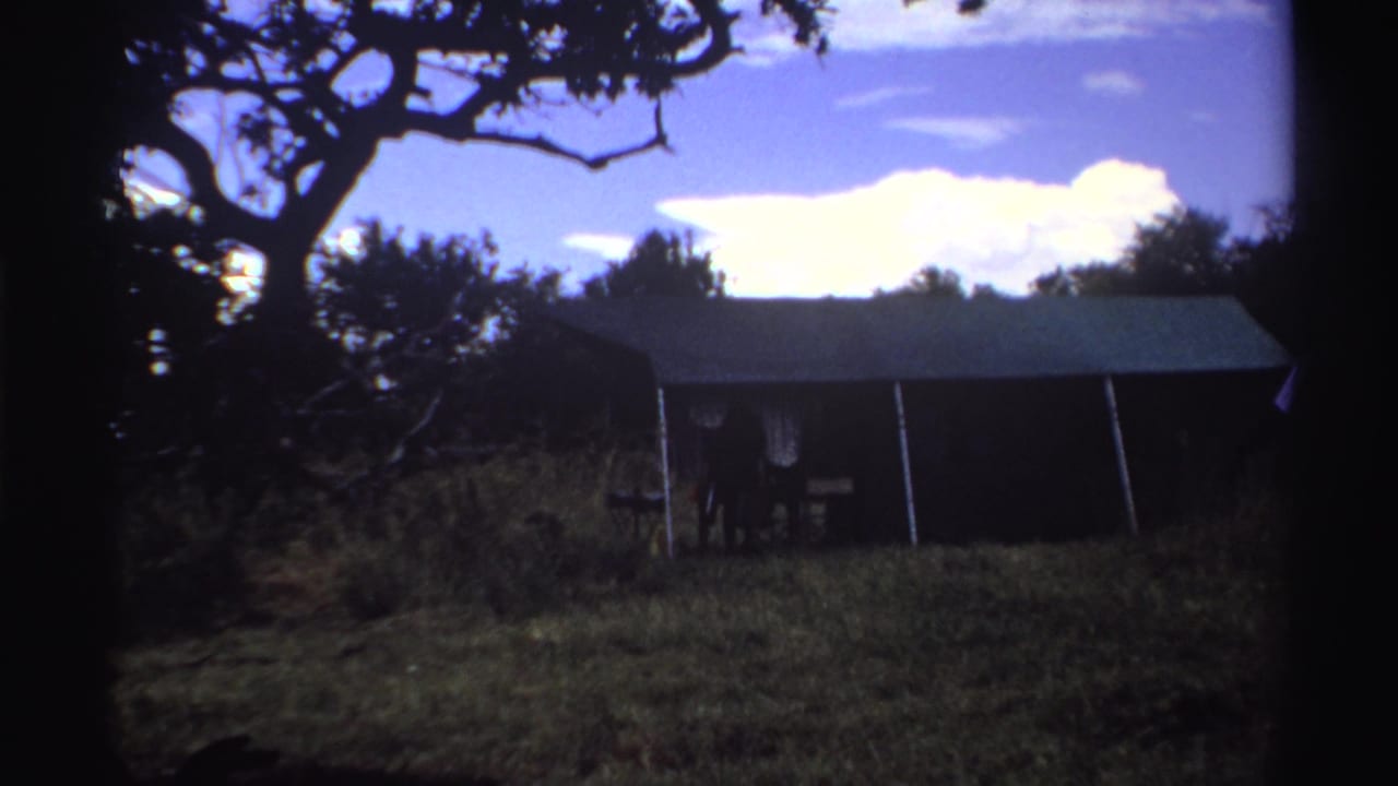 1969 Nigeria 8mm frame showing the shed closer in view, with grass, tree branches, blue sky, and pronounced film borders.