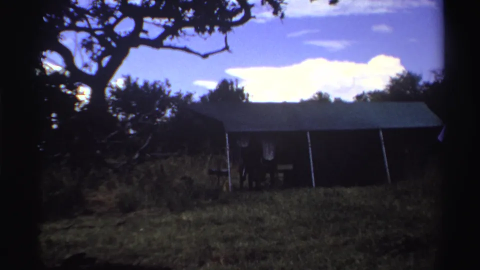 1969 Nigeria 8mm frame showing the shed closer in view, with grass, tree branches, blue sky, and pronounced film borders.