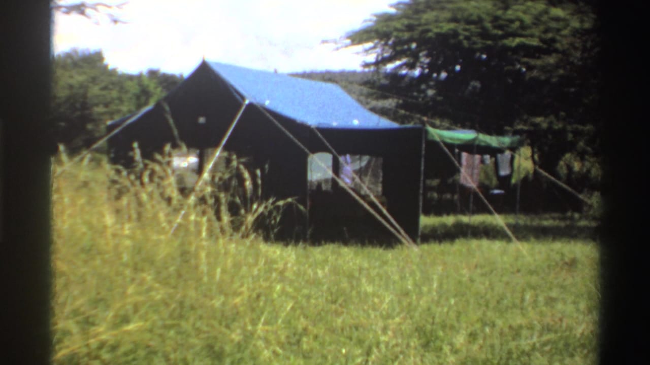 1969 Nigeria 8mm frame showing a large canvas tent in a grassy area with laundry on a line and trees in the background.