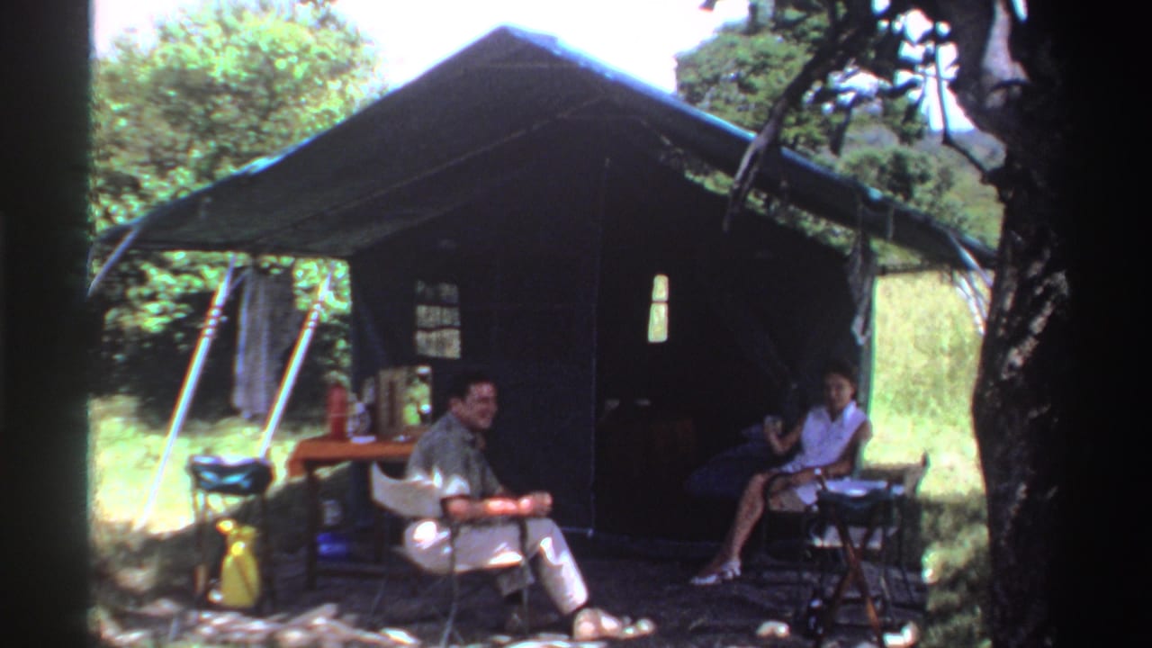 In the final frame, the man remains seated before the tent while the woman gestures beside the table in the wooded camp.