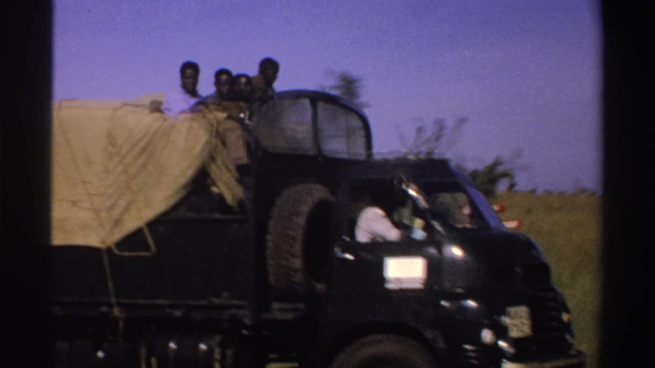 Black covered truck passes close by with several people riding above the tarp.