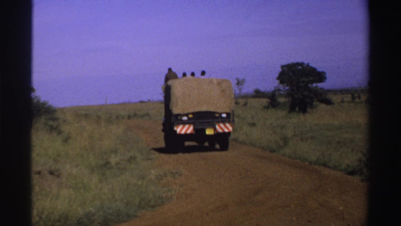 Truck farther down a rural dirt road with grass and trees around it.