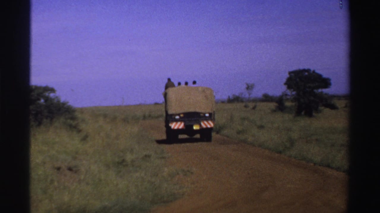 A distant tan truck drives away through open Nigerian countryside, framed by 8mm film borders and saturated daylight color.