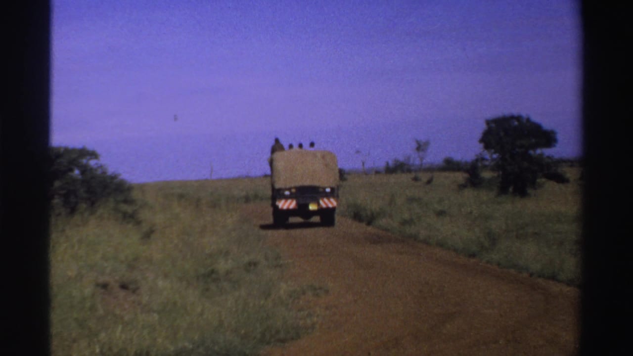 Final frame of the 1969 Nigeria clip with the truck small in the distance on a reddish dirt road through sparse grass and trees.